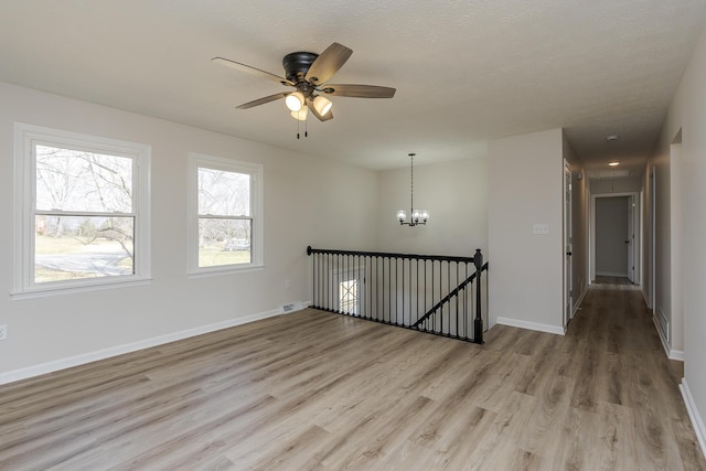 empty room featuring light wood-style flooring, visible vents, baseboards, and ceiling fan with notable chandelier