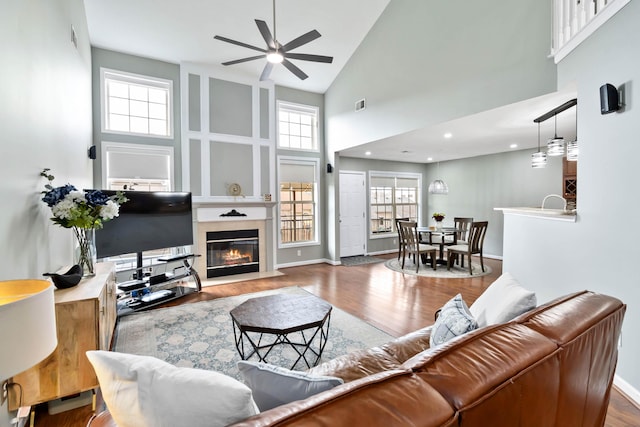 living room featuring ceiling fan, a large fireplace, wood-type flooring, and a high ceiling