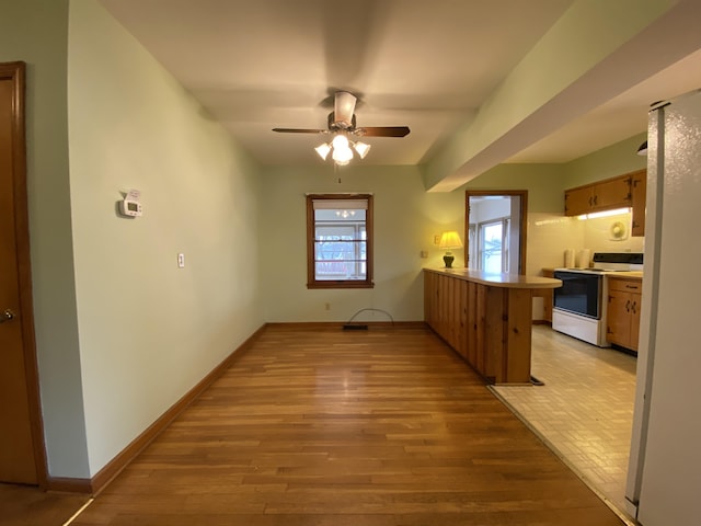 interior space with light hardwood / wood-style flooring, white electric stove, kitchen peninsula, and ceiling fan