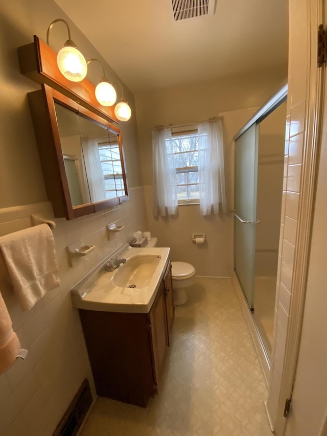 bathroom featuring vanity, a healthy amount of sunlight, tile walls, and a shower with shower door