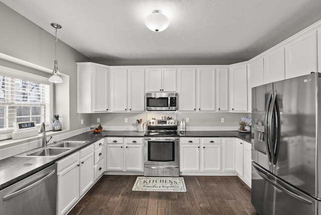 kitchen with appliances with stainless steel finishes, sink, pendant lighting, and white cabinets