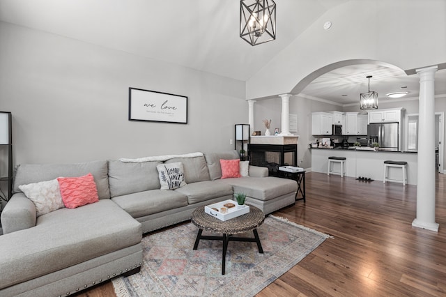 living area featuring arched walkways, a chandelier, dark wood-style flooring, ornate columns, and high vaulted ceiling