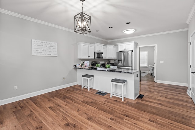 kitchen featuring white cabinets, dark countertops, ornamental molding, a peninsula, and stainless steel appliances