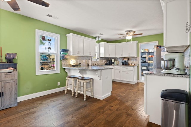 kitchen featuring white cabinetry, backsplash, a kitchen breakfast bar, ceiling fan, and dark wood-type flooring