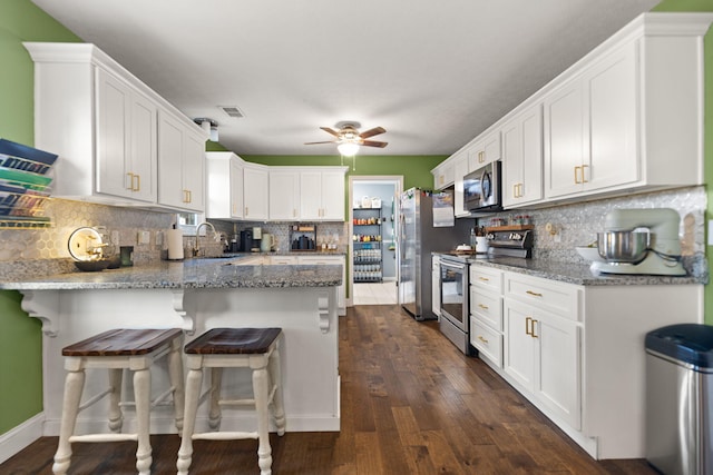 kitchen with light stone counters, a breakfast bar area, white cabinets, and appliances with stainless steel finishes