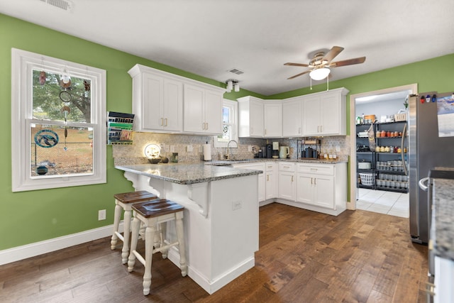 kitchen with stainless steel refrigerator, white cabinetry, a breakfast bar area, light stone counters, and kitchen peninsula