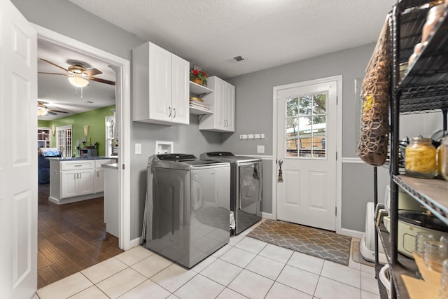 clothes washing area featuring separate washer and dryer, cabinets, light tile patterned floors, ceiling fan, and a textured ceiling