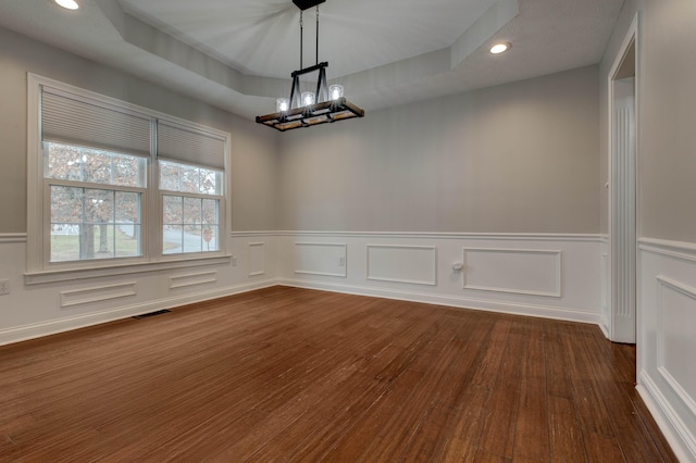 unfurnished dining area featuring dark hardwood / wood-style flooring, a tray ceiling, and a chandelier