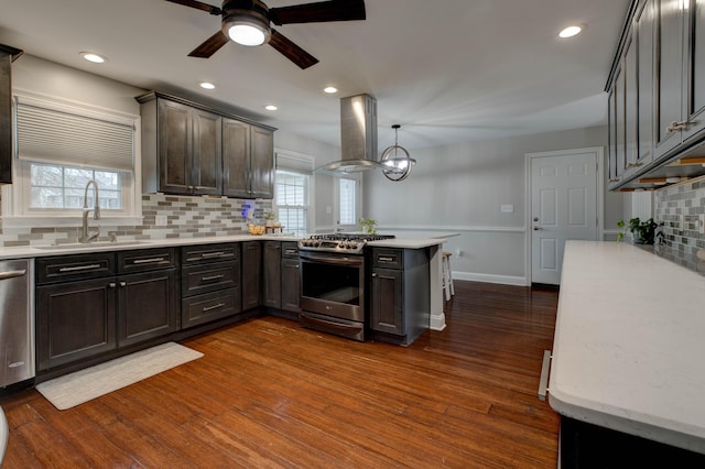 kitchen with appliances with stainless steel finishes, sink, hanging light fixtures, island exhaust hood, and kitchen peninsula