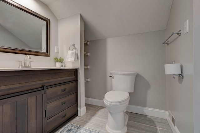 bathroom with hardwood / wood-style flooring, vaulted ceiling, vanity, and toilet