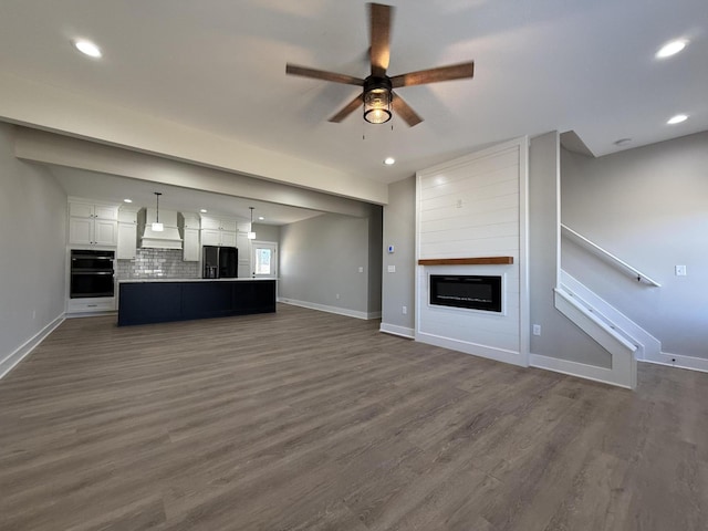 unfurnished living room featuring ceiling fan, dark hardwood / wood-style flooring, and a large fireplace