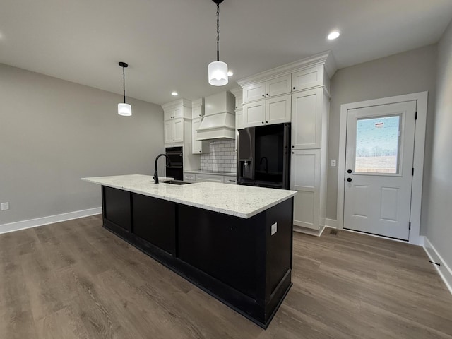 kitchen with custom exhaust hood, white cabinetry, a center island with sink, and black appliances