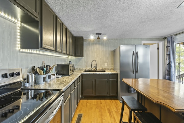 kitchen featuring sink, light hardwood / wood-style flooring, stainless steel appliances, light stone counters, and a textured ceiling