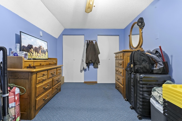 bedroom featuring dark carpet, a textured ceiling, vaulted ceiling, and multiple closets