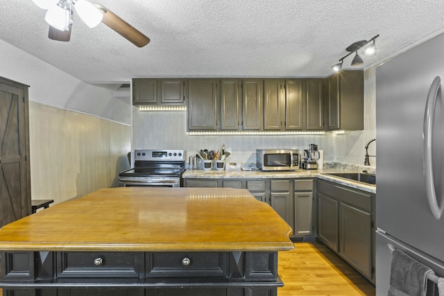 kitchen with appliances with stainless steel finishes, sink, light hardwood / wood-style flooring, and a textured ceiling