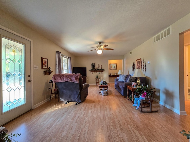 living room featuring ceiling fan, light hardwood / wood-style floors, and a textured ceiling