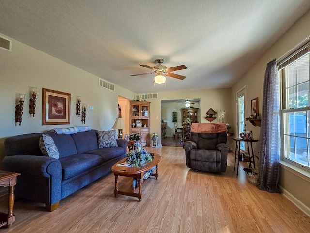 living room with ceiling fan, a textured ceiling, and light wood-type flooring