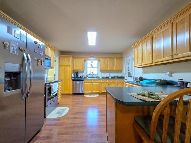 kitchen featuring sink, light hardwood / wood-style flooring, a breakfast bar, appliances with stainless steel finishes, and light brown cabinetry