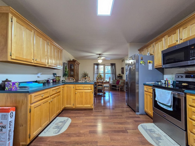 kitchen with dark wood-type flooring, ceiling fan, appliances with stainless steel finishes, and kitchen peninsula