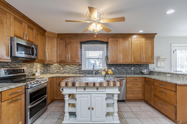 kitchen with stainless steel appliances, light tile patterned flooring, butcher block counters, and sink