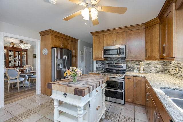 kitchen featuring stainless steel appliances, light tile patterned floors, wooden counters, and decorative backsplash