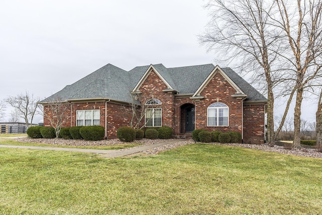 traditional home featuring brick siding, a front yard, and a shingled roof