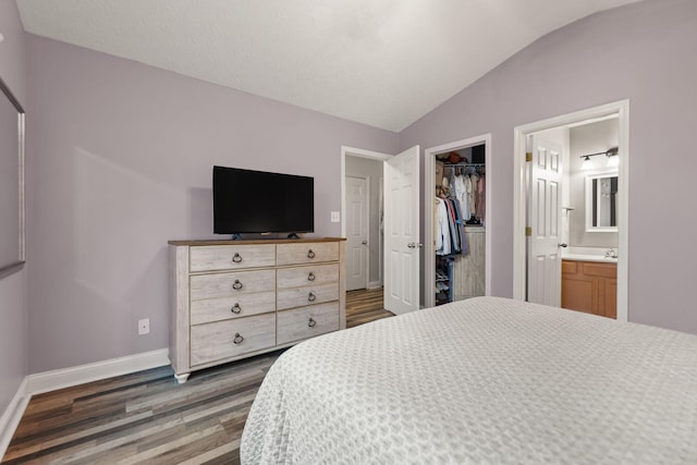 bedroom with lofted ceiling, dark hardwood / wood-style floors, connected bathroom, a walk in closet, and a closet