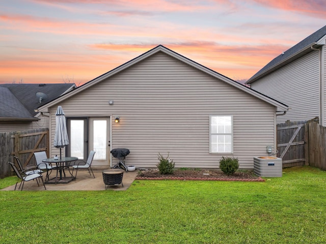 back house at dusk featuring a yard, a patio area, and central air condition unit