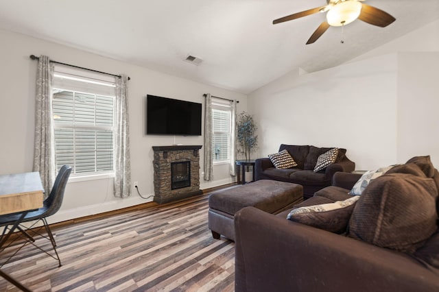 living room with vaulted ceiling, a stone fireplace, hardwood / wood-style floors, and ceiling fan