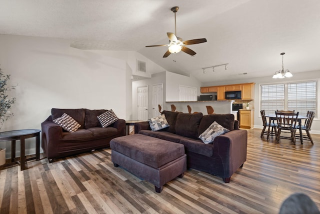 living room featuring vaulted ceiling, ceiling fan with notable chandelier, rail lighting, dark wood-type flooring, and a textured ceiling