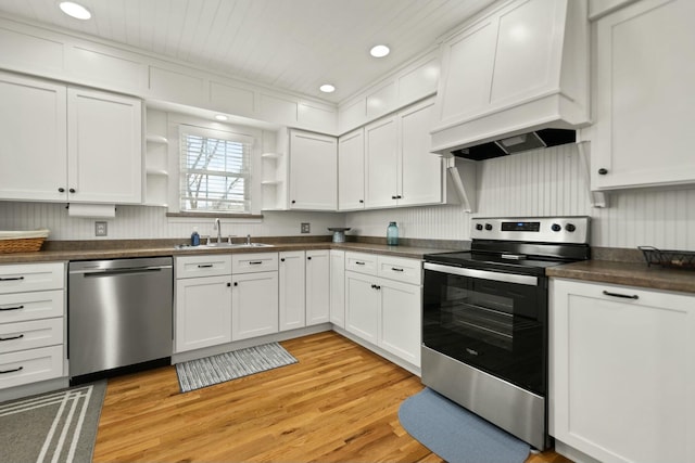 kitchen with open shelves, dark countertops, custom range hood, appliances with stainless steel finishes, and a sink