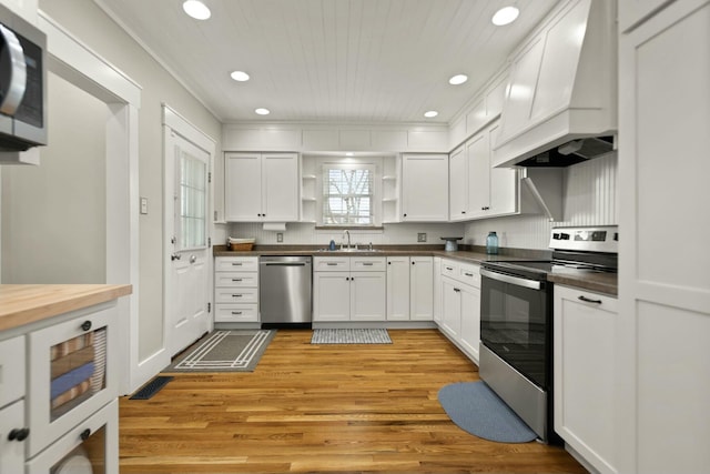 kitchen featuring custom range hood, stainless steel appliances, light wood-style floors, open shelves, and a sink