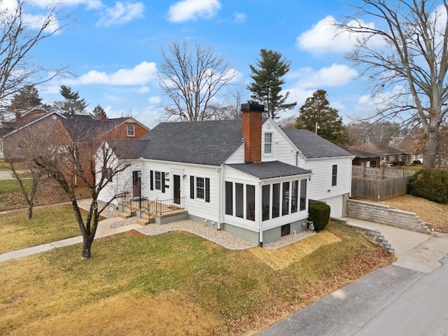 view of front of home with a chimney, a sunroom, a garage, driveway, and a front lawn