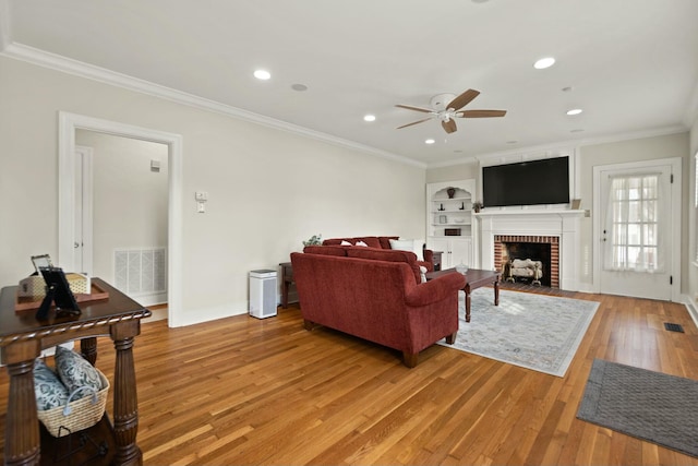 living area with light wood-style flooring, recessed lighting, a fireplace, visible vents, and crown molding