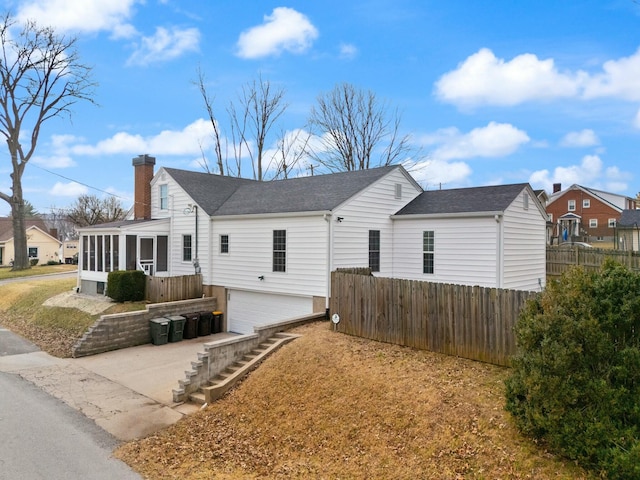 exterior space with a chimney, concrete driveway, an attached garage, a sunroom, and fence