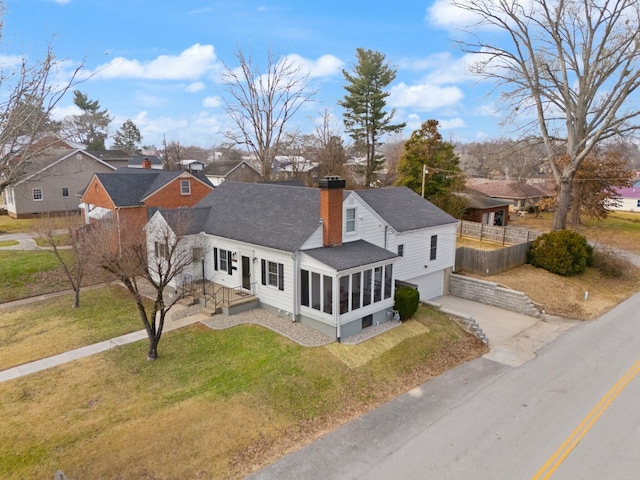 view of front of property with a chimney, concrete driveway, an attached garage, a sunroom, and fence