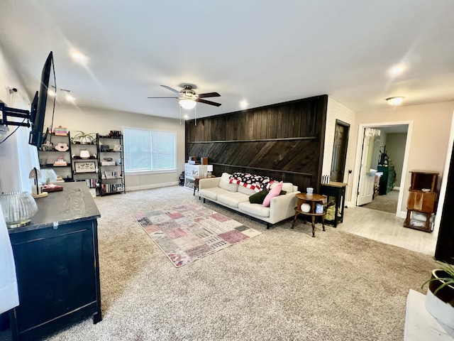 carpeted living room featuring ceiling fan and wood walls