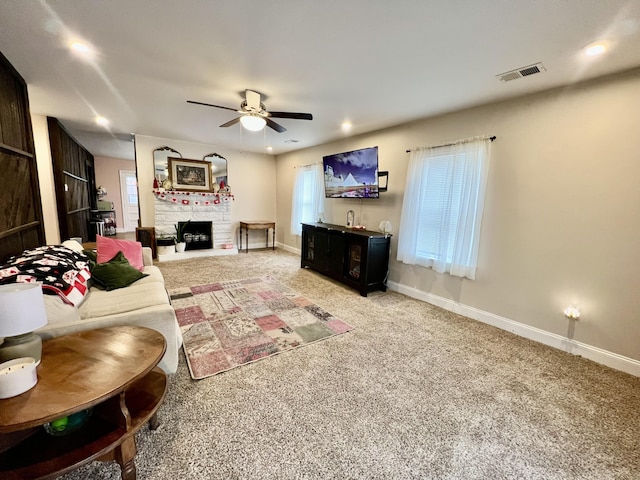 living room with a stone fireplace, carpet, and ceiling fan