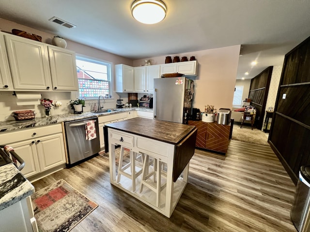 kitchen featuring sink, appliances with stainless steel finishes, white cabinetry, wood-type flooring, and light stone countertops