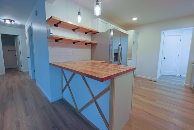 kitchen with butcher block countertops, a kitchen breakfast bar, hanging light fixtures, kitchen peninsula, and stainless steel refrigerator with ice dispenser