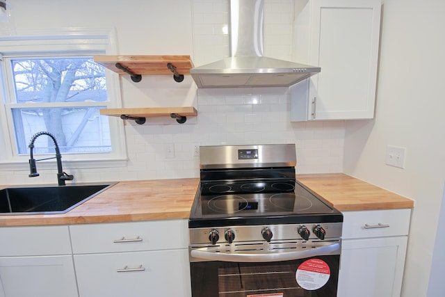 kitchen featuring butcher block counters, sink, wall chimney exhaust hood, and stainless steel electric range oven