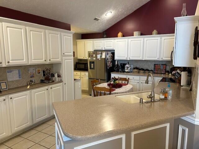 kitchen with sink, white cabinetry, black microwave, light tile patterned floors, and an island with sink