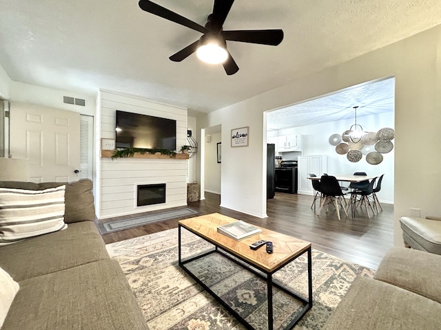 living room featuring dark wood-type flooring, a fireplace, and ceiling fan with notable chandelier