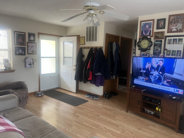 living room featuring ceiling fan, light hardwood / wood-style flooring, and a textured ceiling