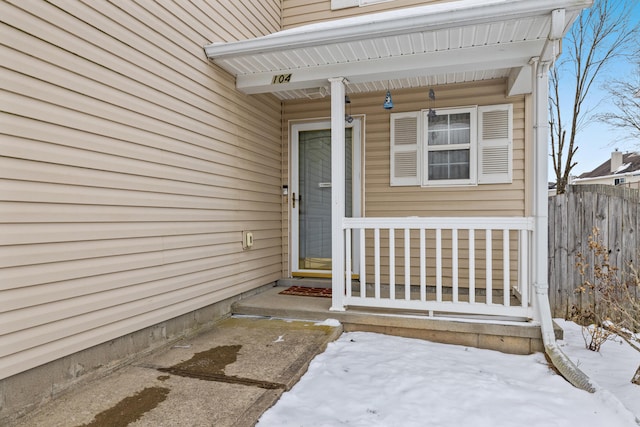 snow covered property entrance with covered porch and fence