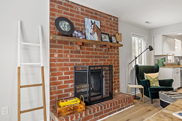 living room featuring crown molding, a brick fireplace, sink, and light hardwood / wood-style flooring