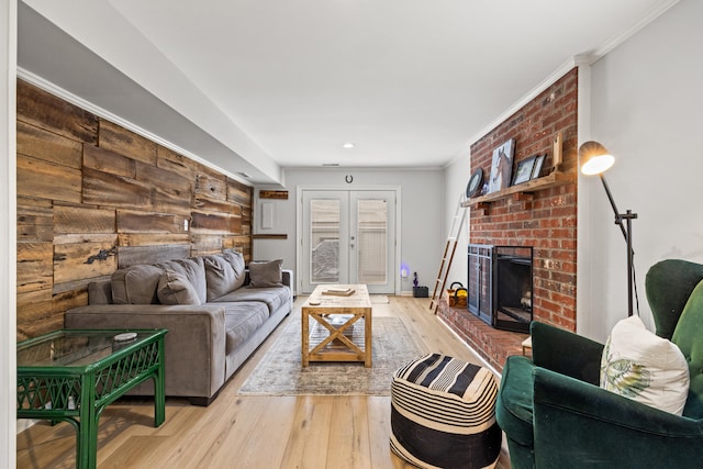 living room featuring french doors, ornamental molding, a brick fireplace, and light hardwood / wood-style flooring