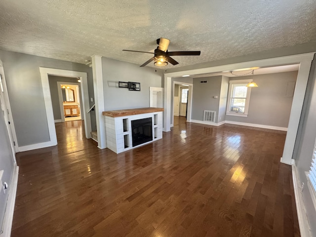 unfurnished living room featuring ceiling fan, dark wood-type flooring, and a textured ceiling