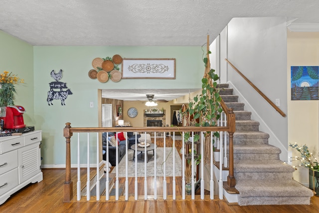 stairs featuring ceiling fan, a fireplace, hardwood / wood-style floors, and a textured ceiling