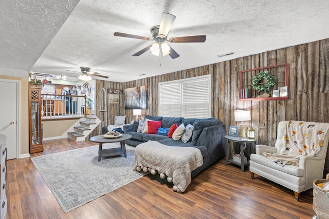 living room with ceiling fan, dark wood-type flooring, a textured ceiling, and wood walls